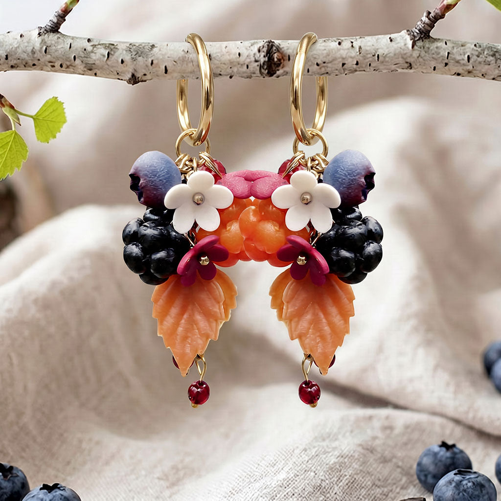 Marjametsä earrings with gold-colored Huggie hoops, photographed on a birch branch in soft natural light