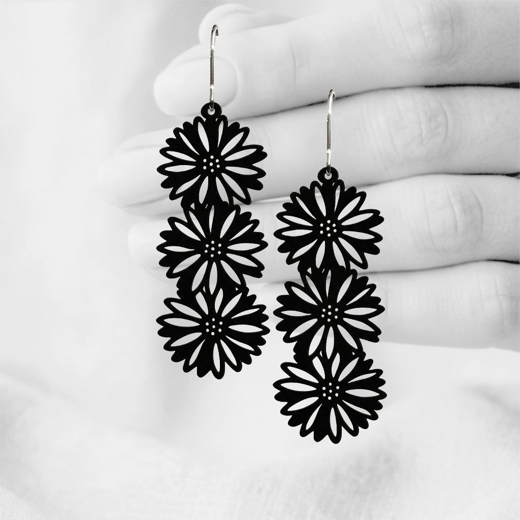 Black Asteria silicone earrings made in Finland, photographed against a black and white background of a hand.