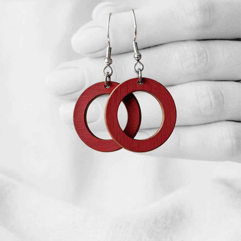 Rust Red Circle plywoodearrings made in Finland, photographed hanging from a hand in black and white against a softly blurred light background.