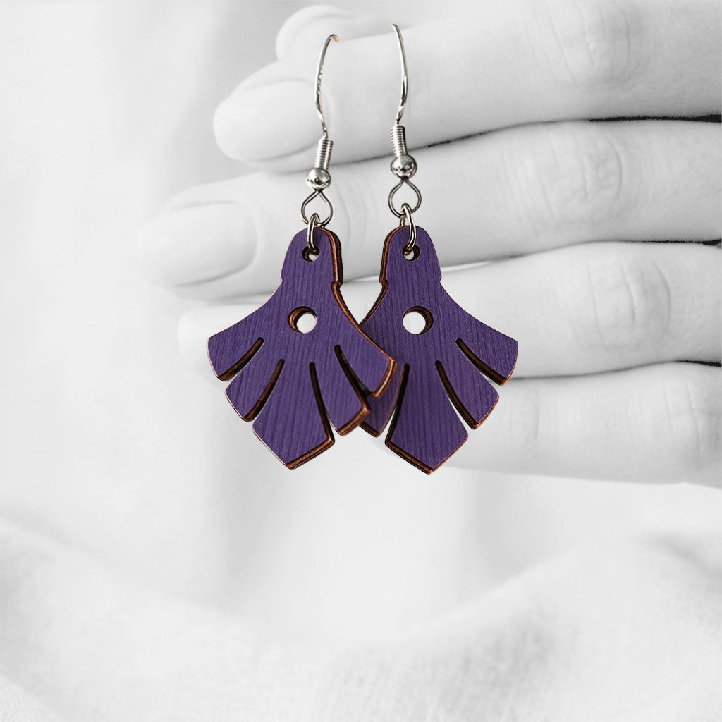 Plum Phoenix plywood earrings made in Finland, photographed hanging from a hand in black and white against a softly blurred light background.