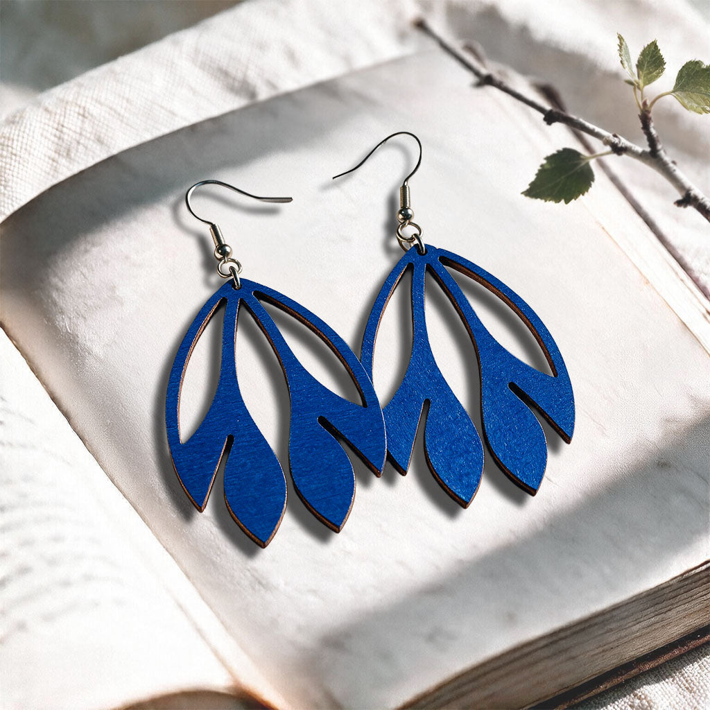 Blue Flutter plywood earrings made in Finland, photographed on a vintage book in natural sunlight