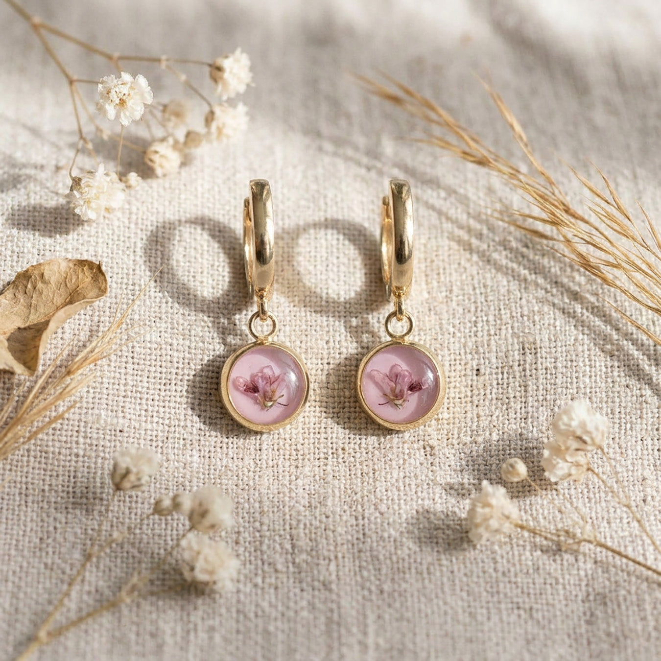 Delicate pink heather flower huggie earrings styled with dried flowers on linen fabric, handmade in Finland