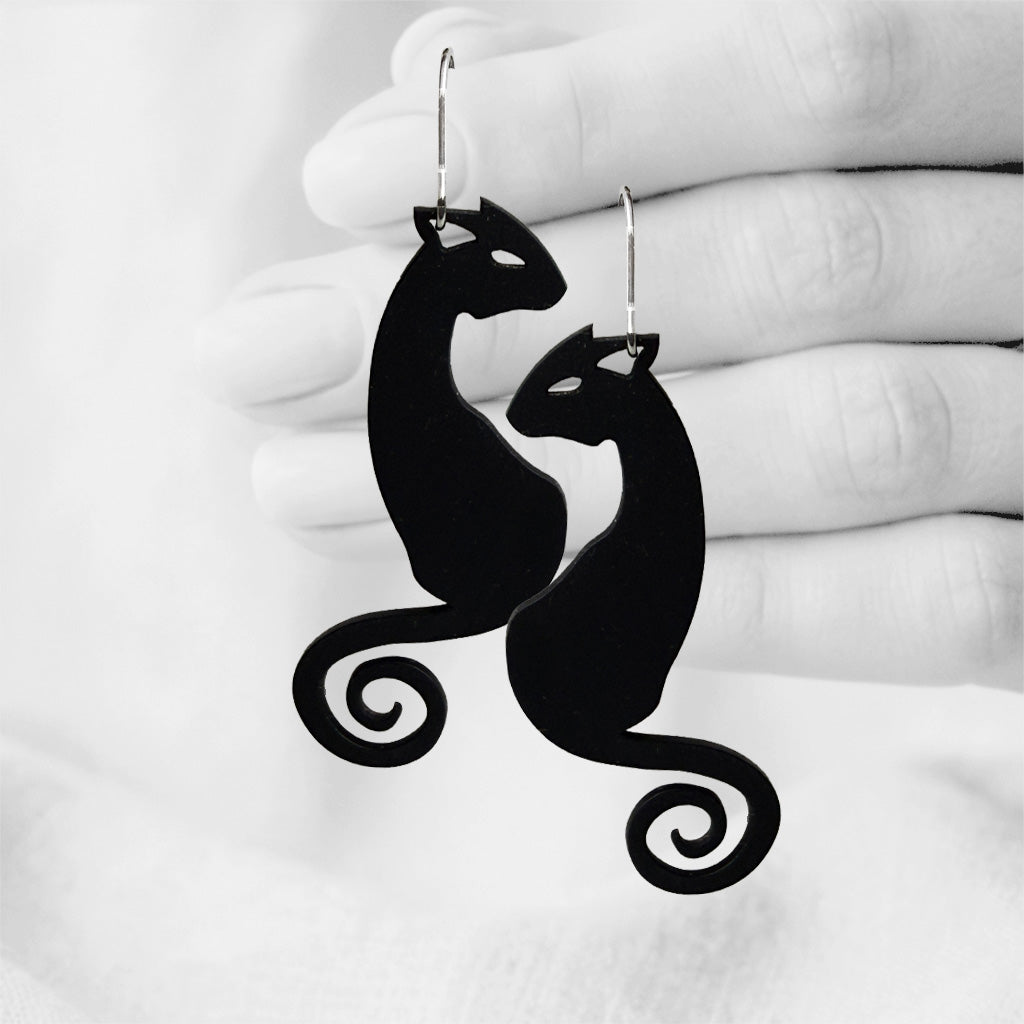 Black Kattimus (Cat) silicone earrings made in Finland, photographed against a black and white background of a hand.