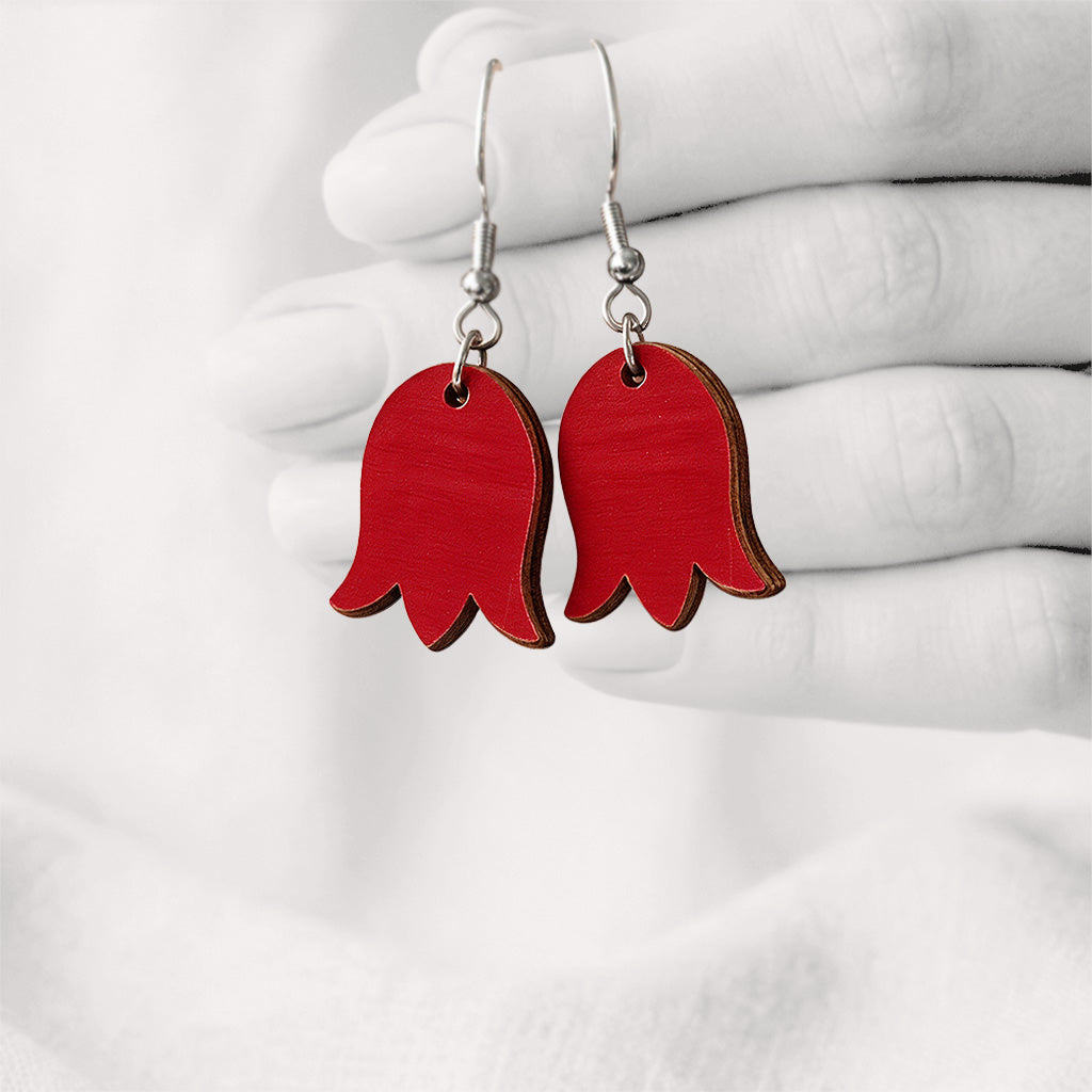 Blue bellflower-shaped plywood earrings handmade in Finland, hanging from a hand against a softly blurred light linen background.