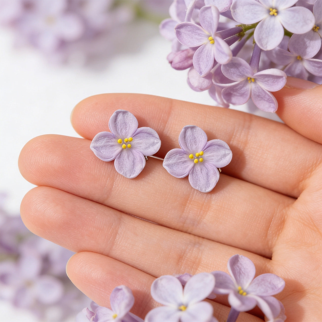 handmade lilac flower stud earrings on hand with lilac blossoms background byMinta