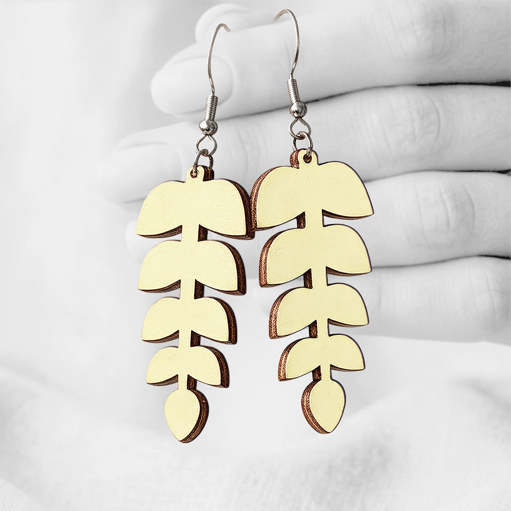 Lehdykkä (Leaflet) plywood earrings made in Finland, photographed hanging from a hand in black and white against a softly blurred light background.