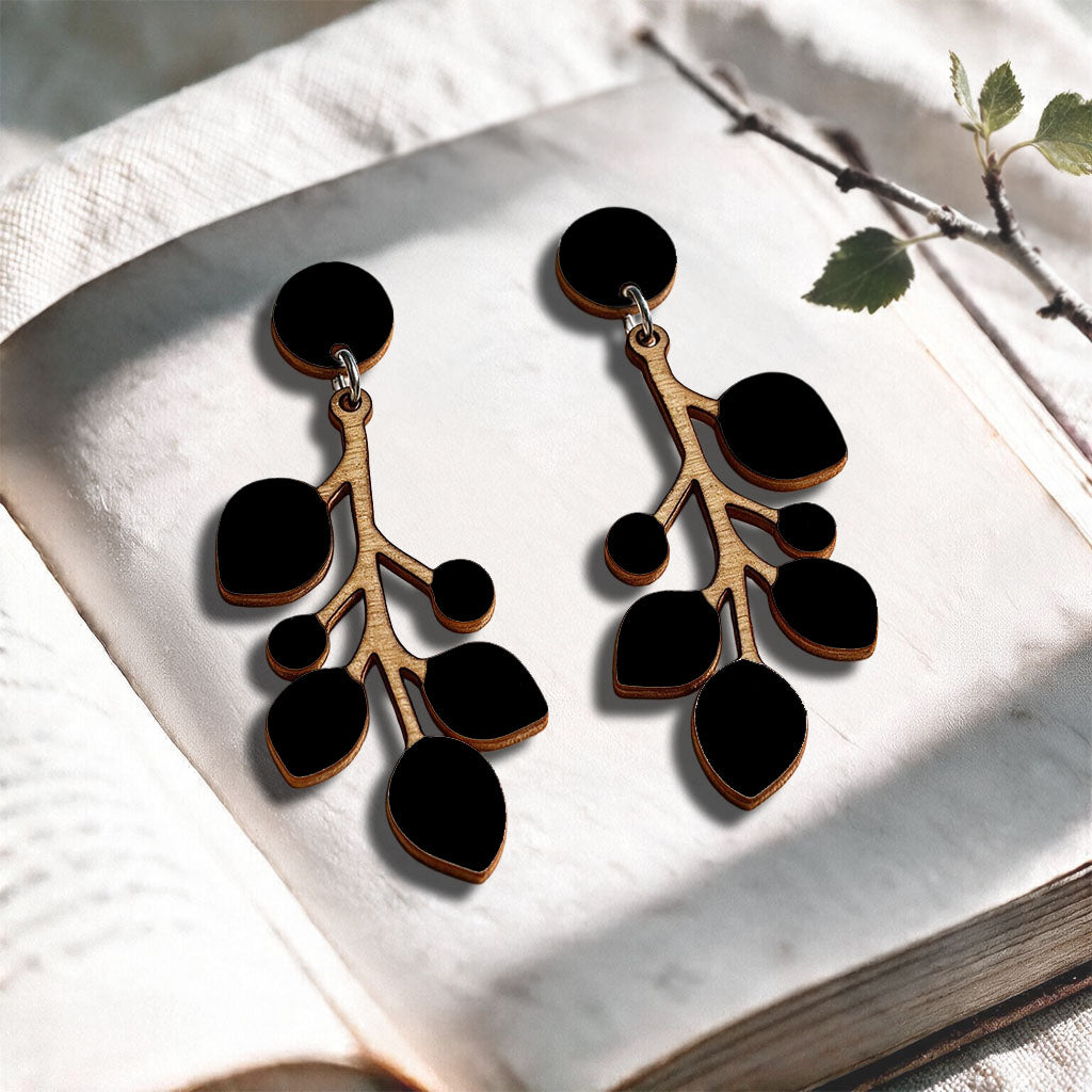Black Snowberry stud plywood earrings made in Finland, photographed on a vintage book in natural sunlight