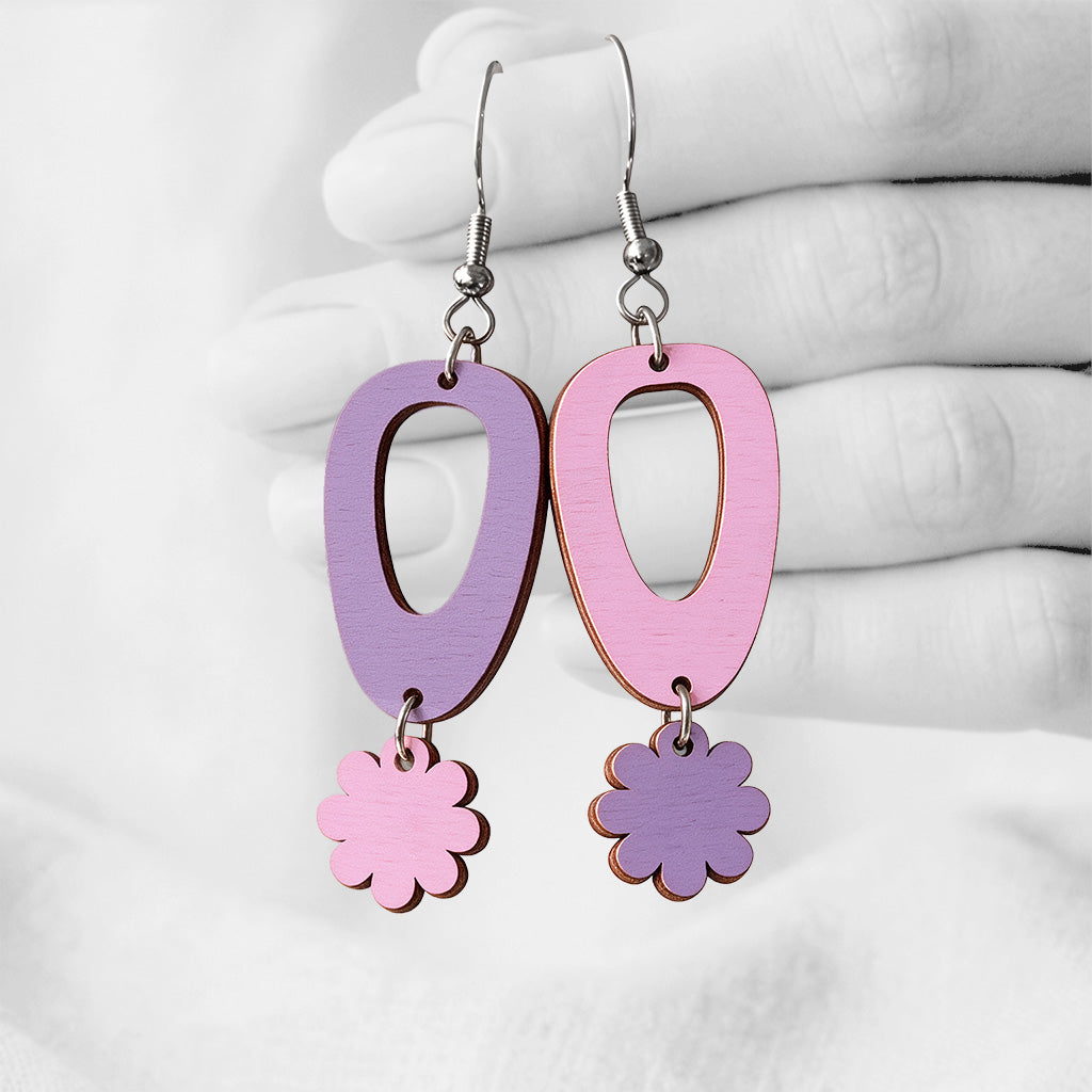 Amethyst and mauve Luotokukka (Islet Flower) plywood earrings made in Finland, photographed against a black and white background of a hand.