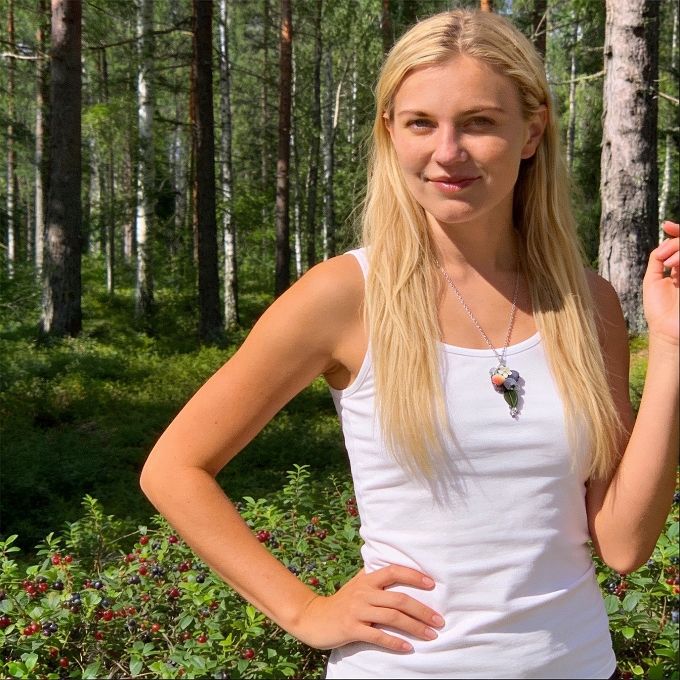 Blonde woman wearing the Blueberry Branch Necklace in a sunlit Nordic forest. Handmade necklace with hand-shaped blueberries and leaves, photographed in natural summer light. Handmade in Finland by byMinta.