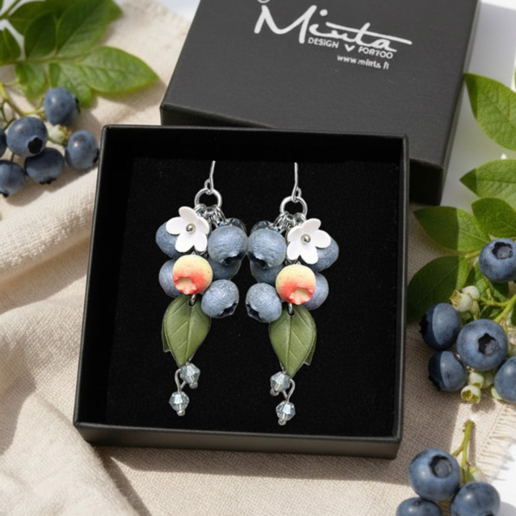Blueberry Branch Earrings presented in a gift box, surrounded by natural linen fabric, fresh blueberries, and blueberry leaves. Handmade in Finland by byMinta.