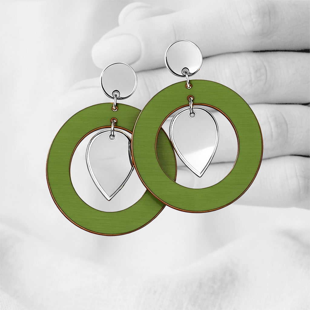 Green NiinMua plywood stud earrings with silver mirror acrylic teardrops, made in Finland, photographed against a black-and-white hand background.