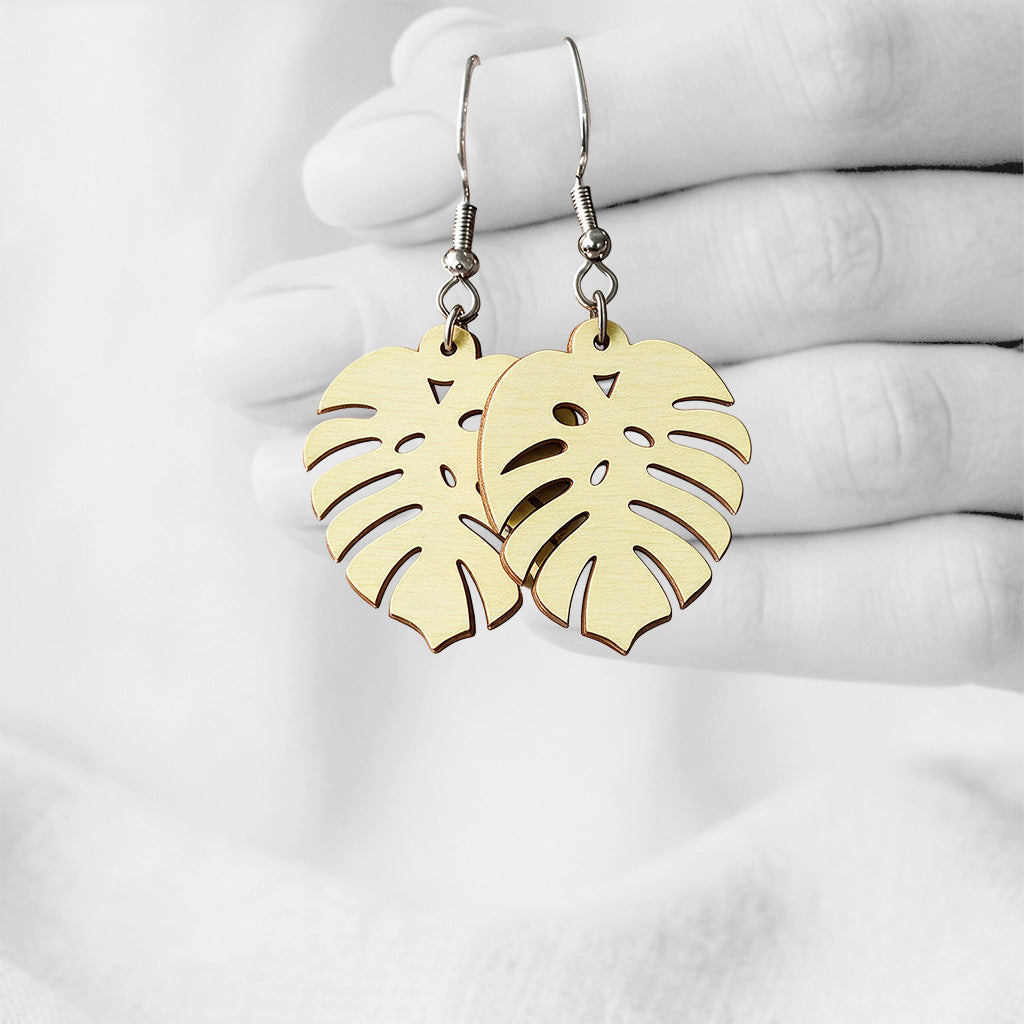 Vanilla Vehreä (Verdant) plywood earrings made in Finland, photographed on a vintage book in natural sunlight plywood earrings handmade in Finland, photographed hanging against a black-and-white hand background.