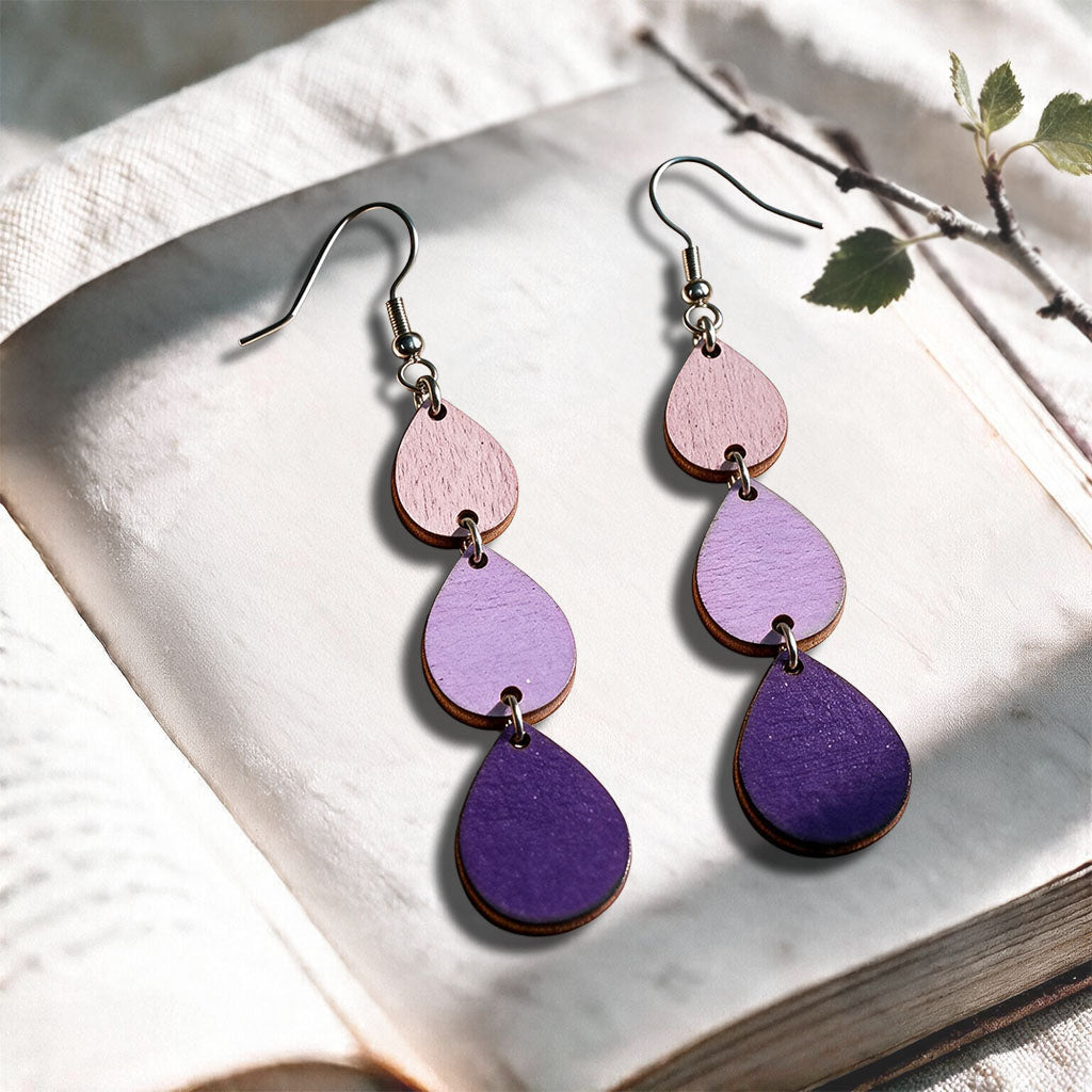 Purple Raindrops plywood earrings made in Finland, photographed on a vintage book in natural sunlight