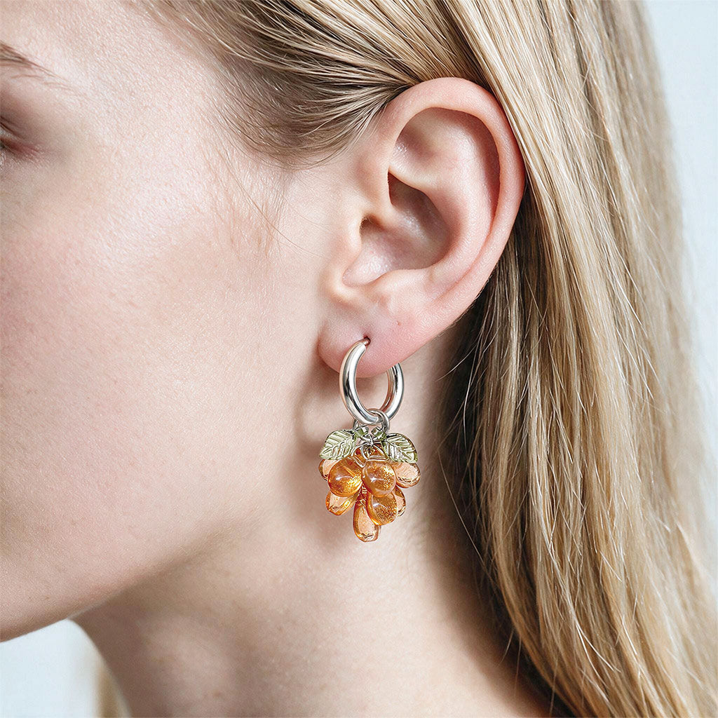 Handmade orange glass cluster earrings with stainless steel huggie hoops, made in Finland and shown on the ear of a woman.