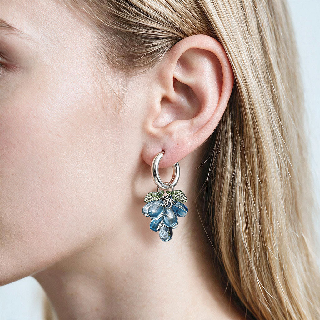 Handmade blue glass cluster earrings with stainless steel huggie hoops, shown on the ear of a woman, made in Finland.