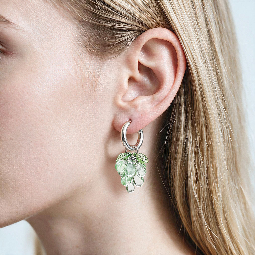 Handmade green glass cluster earrings with stainless steel huggie hoops, made in Finland and shown on the ear of a woman.