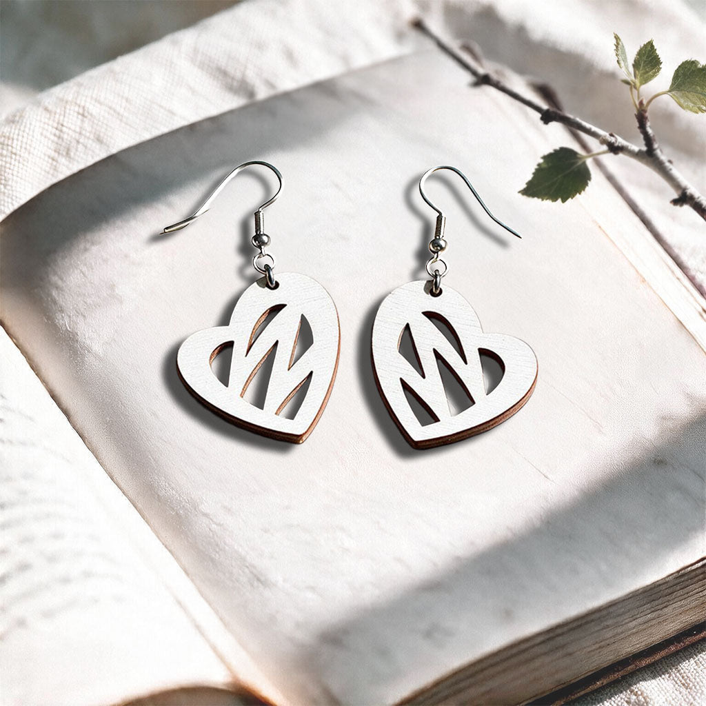 White Heartbeat plywood earrings made in Finland, photographed on a vintage book in natural sunlight