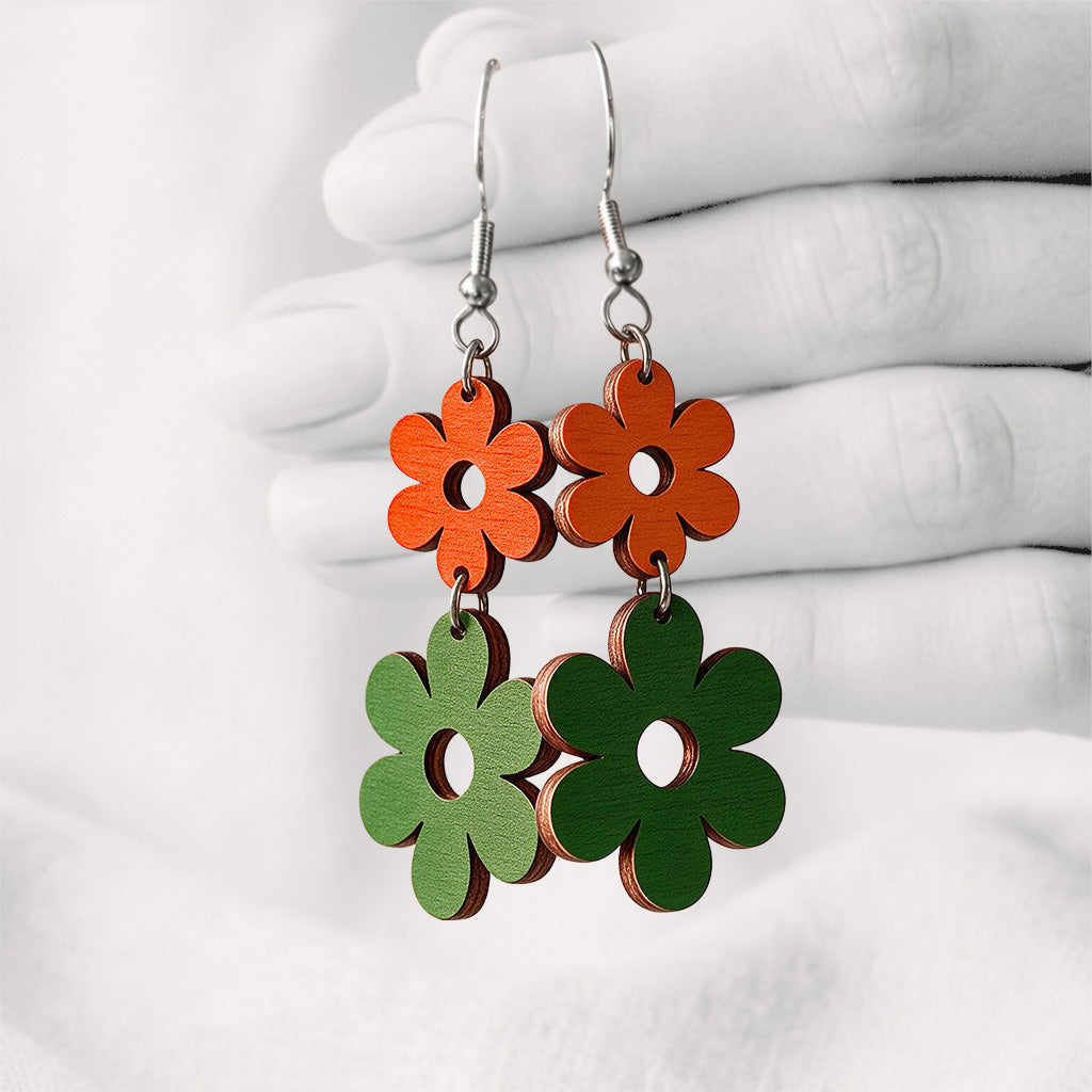 Orange and green TuplaRetro Duo plywood earrings made in Finland, photographed hanging from a hand against a softly blurred light linen background.