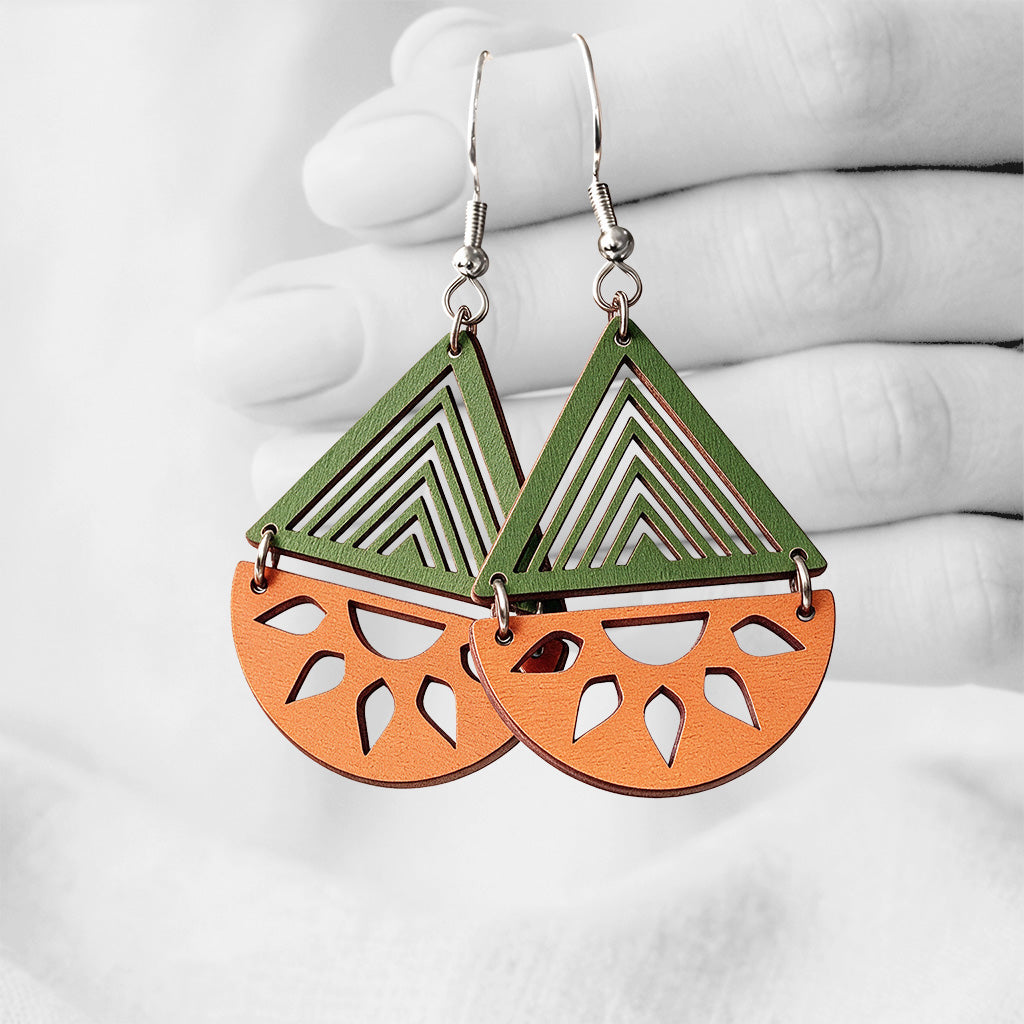 Orange and green Ulappa (Open Sea) plywood earrings made in Finland, photographed against a black and white background of a hand.