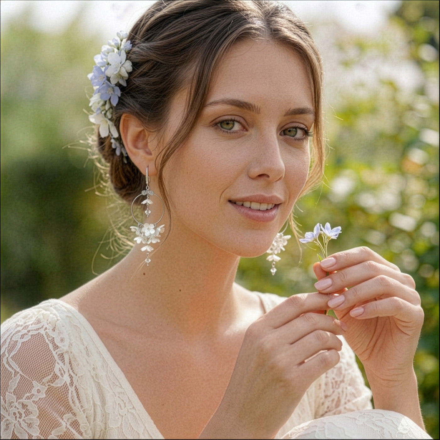Bride in a sunlit summer garden wearing delicate white floral hoop earrings by byMinta. Her hair is styled with white and pale blue flowers, and she wears an ivory lace dress.