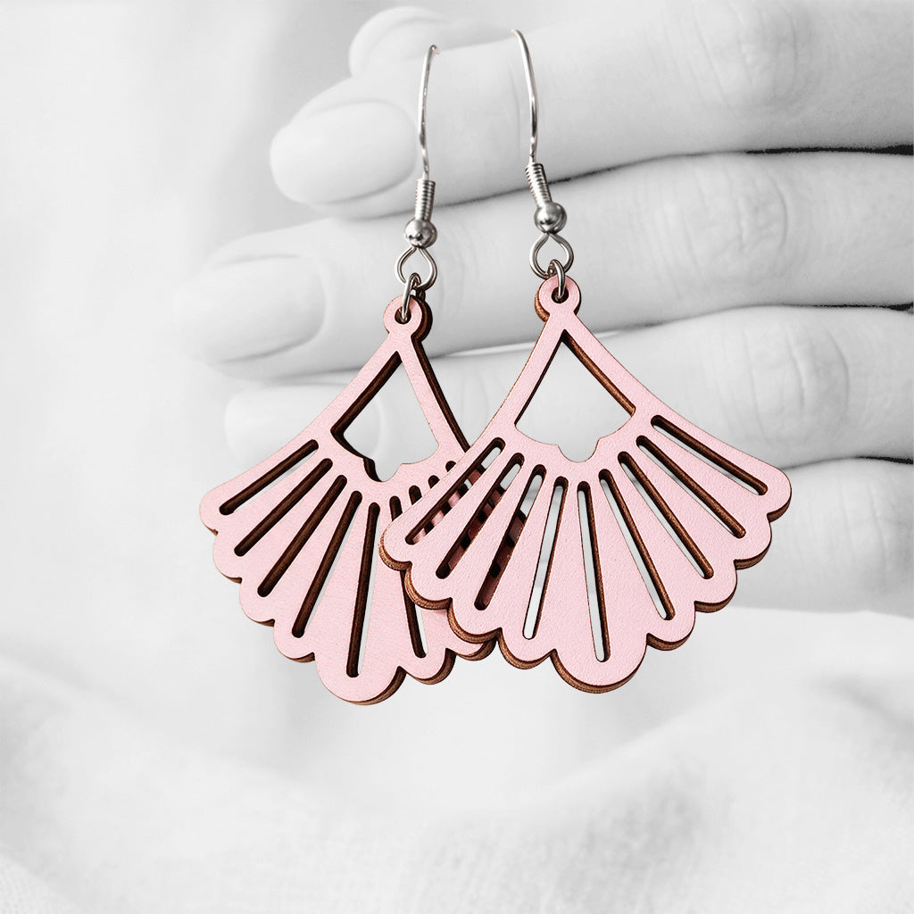 Pink Viuhka (Fan) plywood earrings handmade in Finland, photographed hanging against a black-and-white hand background.
