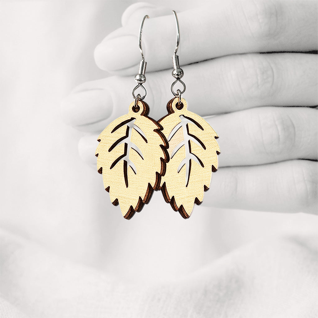 Vanilla Mini Koivu (birch leaf) plywood earrings made in Finland, photographed hanging from a hand against a softly blurred light linen background.
