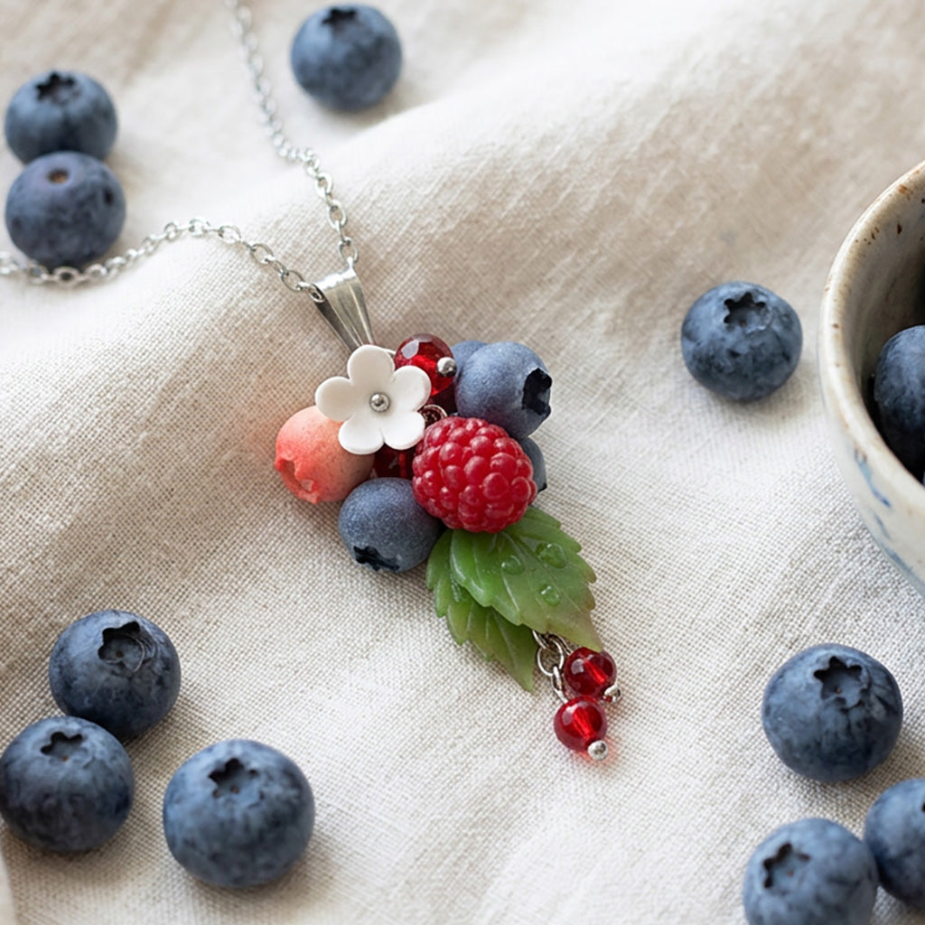 Berry necklace with handmade raspberry, blueberries and white flower on linen fabric, surrounded by fresh blueberries, handcrafted Finnish jewelry.