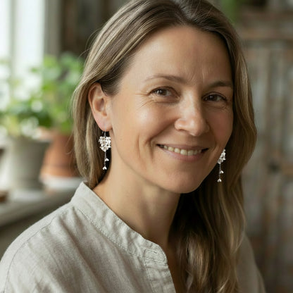 Smiling woman wearing handcrafted white Mock Orange flower earrings made in Finland.