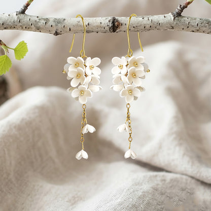 Handcrafted white Jasmike flower earrings hanging from a birch branch on natural linen fabric, made in Finland.