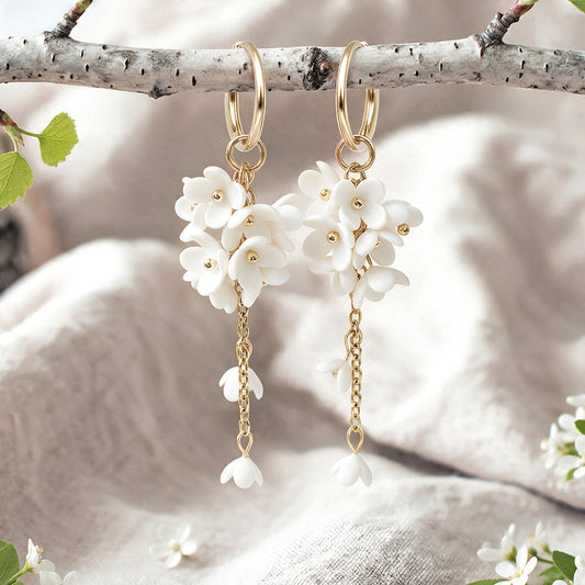 Handcrafted white Jasmike flower earrings hanging from a birch branch on natural linen fabric, made in Finland.