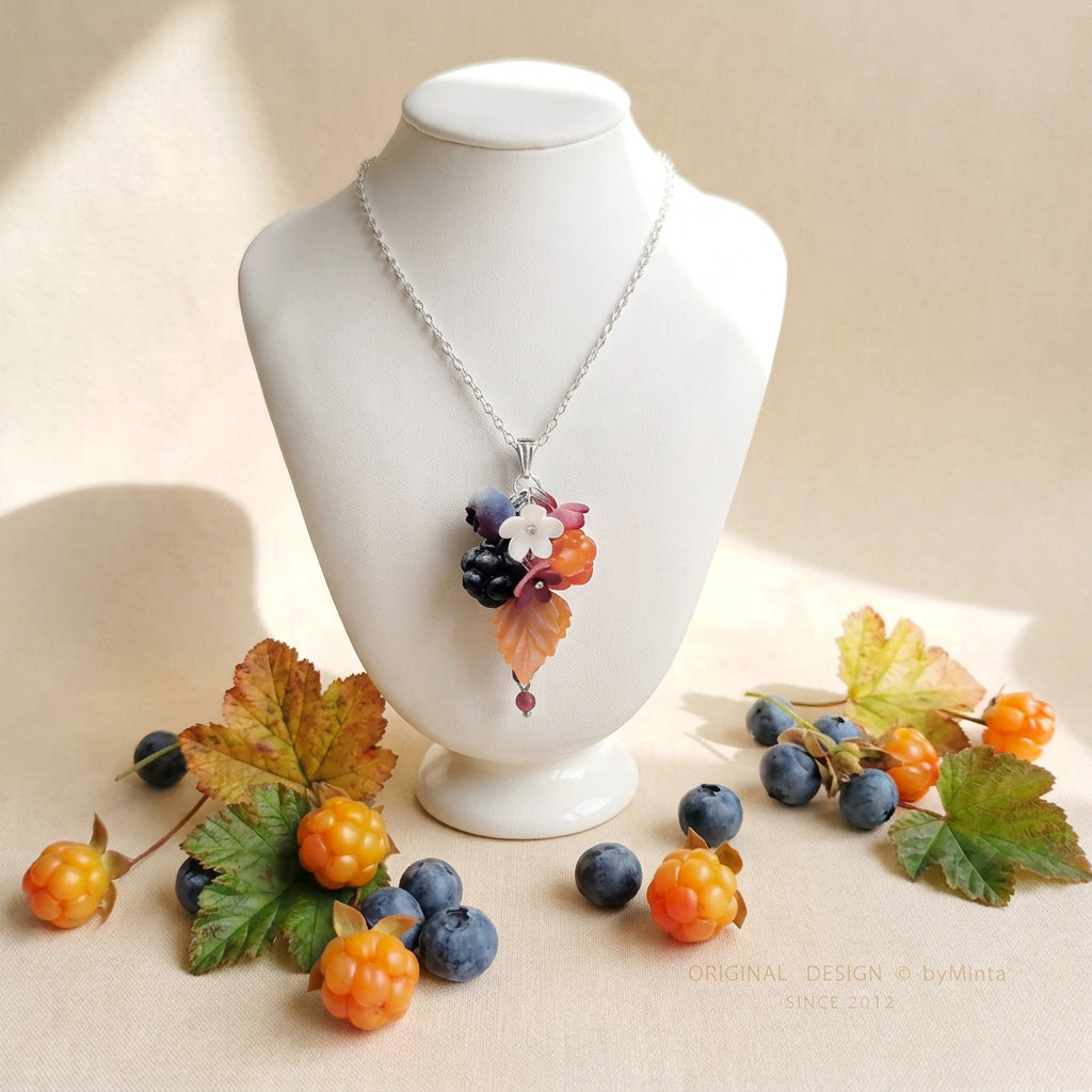 Marjametsä necklace with a stainless steel chain, photographed on a white jewelry display among berries and autumn leaves in natural light