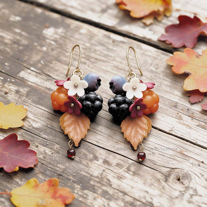 Marjametsä earrings with gold-colored details, handmade in Finland, photographed on a rustic wooden surface with autumn leaves