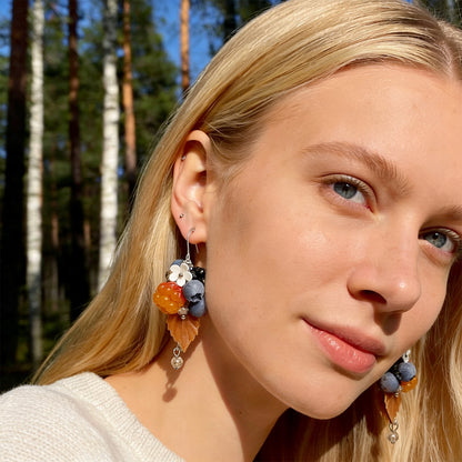 Blonde woman wearing Berry Forest Earrings in a sunlit Nordic forest. Handmade earrings inspired by the rich colors and quiet beauty of northern berries.