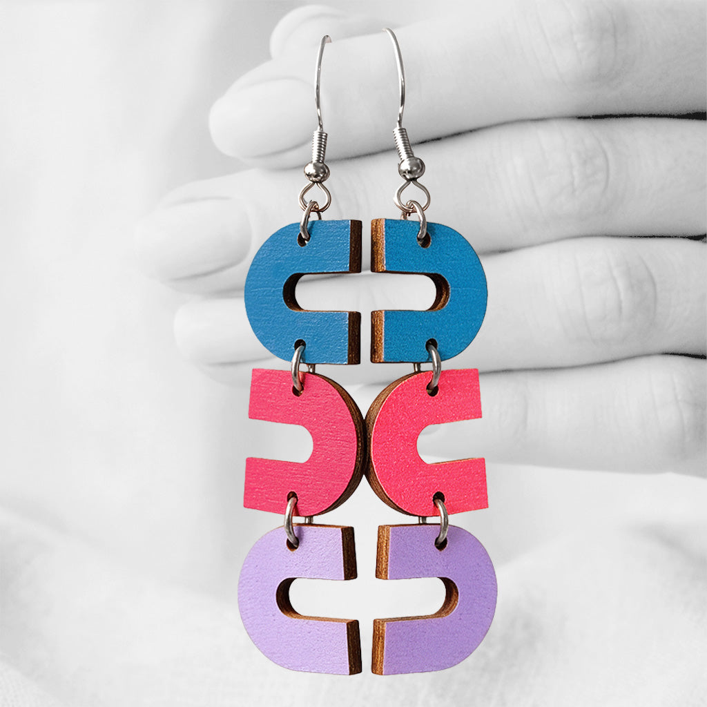 Skyblue, raspberry and lilac Uukkari (U-turn) plywood earrings made in Finland, photographed against a black and white background of a hand.