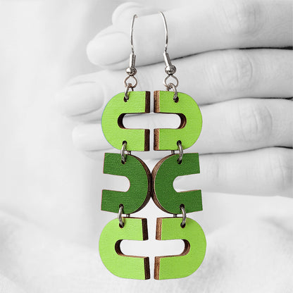 Green and limegreen  Uukkari (U-turn) plywood earrings made in Finland, photographed against a black and white background of a hand.