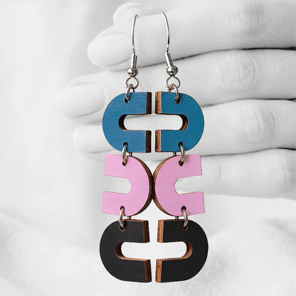 Petrol, mauve and black Uukkari (U-turn) plywood earrings made in Finland, photographed against a black and white background of a hand.