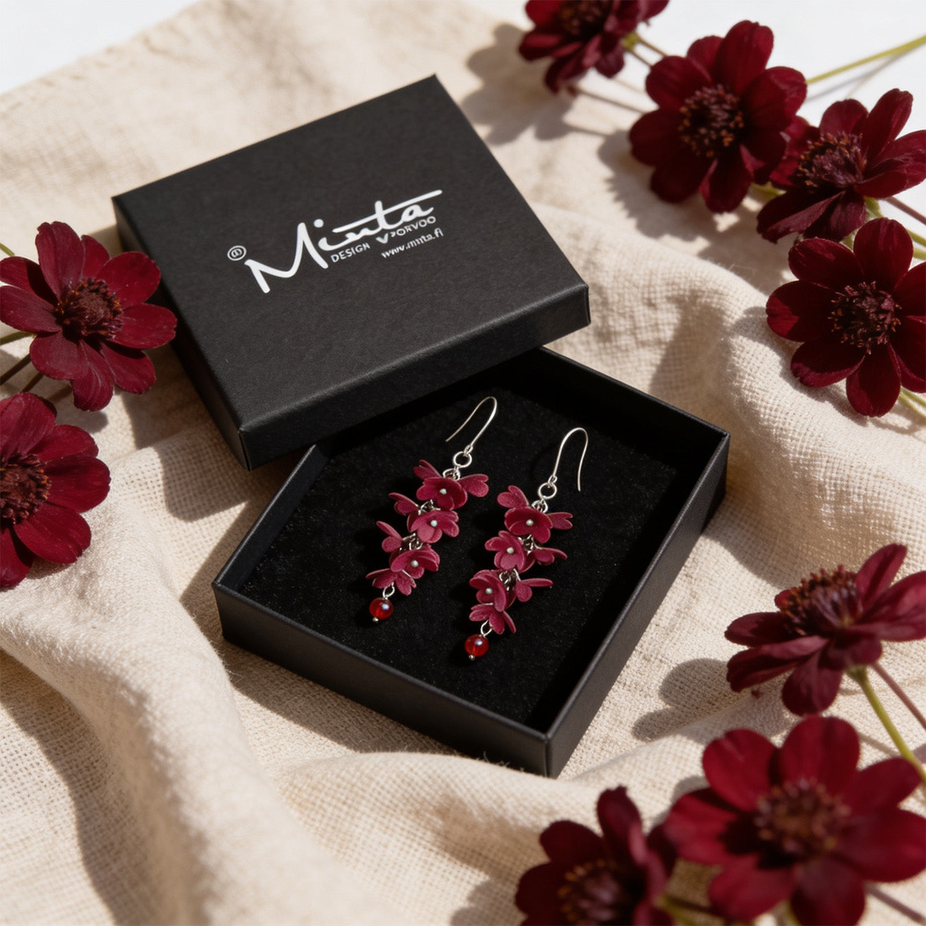 Shadow Vine Burgundy Earrings presented in a gift box, surrounded by natural linen fabric and burgundy flowers. Handmade in Finland by byMinta.