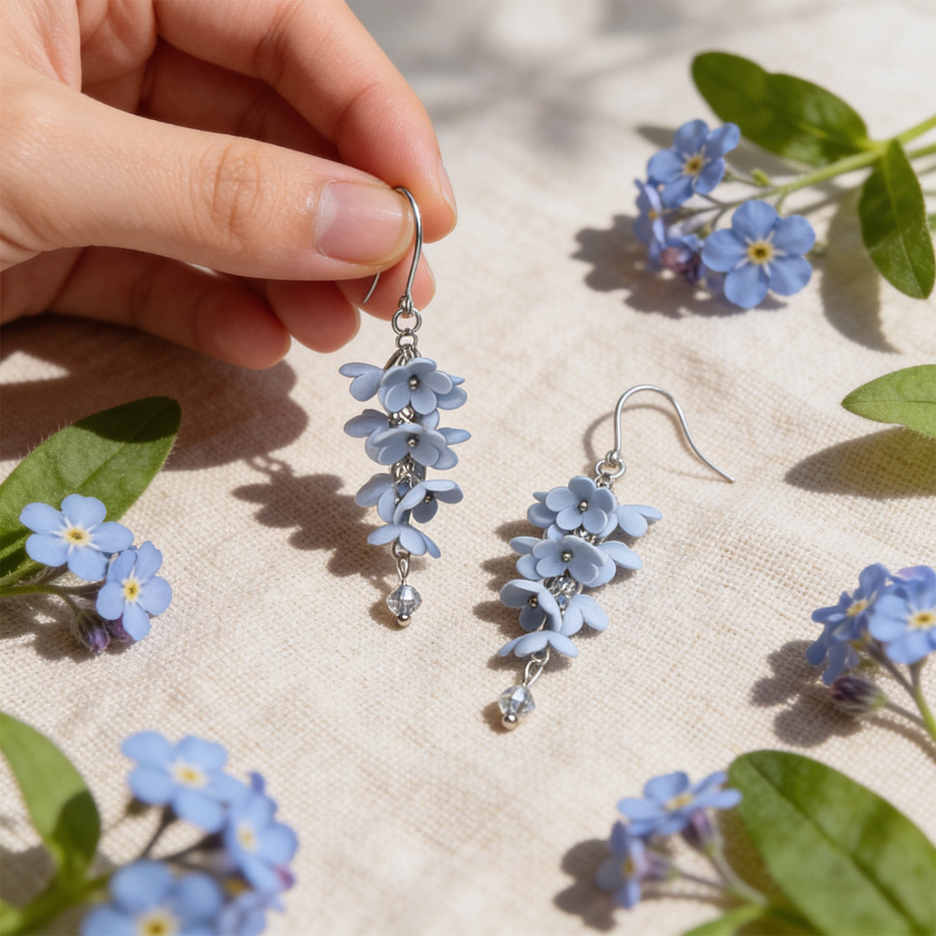 hadow Vine Earrings photographed with forget-me-nots in soft natural light, with one earring gently held by hand for scale. Handmade in Finland by byMinta.