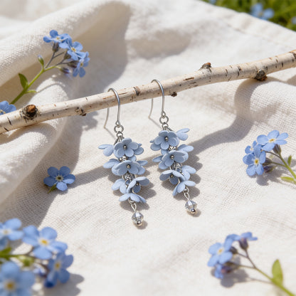 Shadow Vine Earrings displayed on a birch branch among forget-me-nots in bright natural daylight. Handmade in Finland by byMinta.