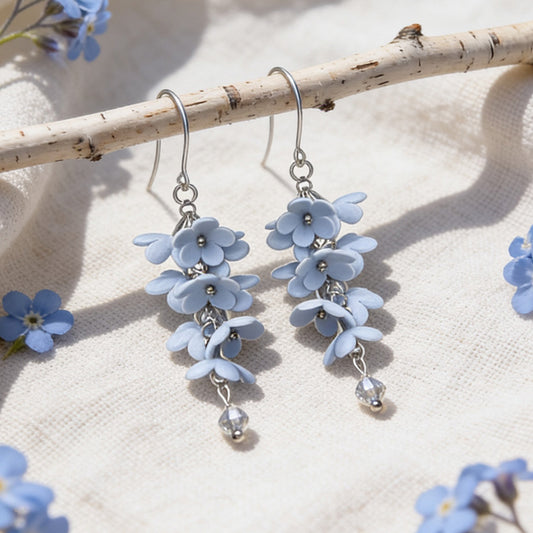 Shadow Vine Earrings displayed on a birch branch among forget-me-nots in bright natural daylight. Handmade in Finland by byMinta.