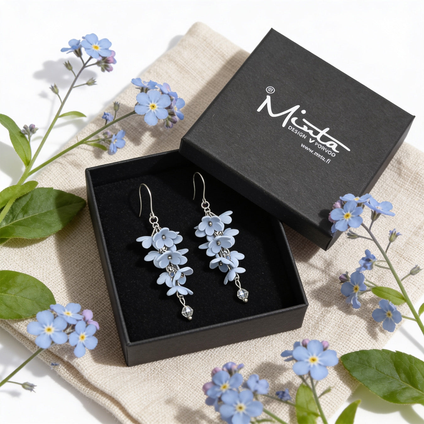 Shadow Vine Earrings presented in a gift box, surrounded by natural linen fabric and delicate blue flowers. Handmade in Finland by byMinta.