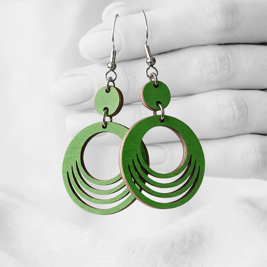 Green Väre (Ripple) plywood earrings made in Finland, photographed against a black and white background of a hand.
