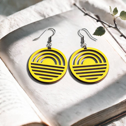 Yellow Sunrise plywood earrings made in Finland, photographed on a vintage book in natural sunlight