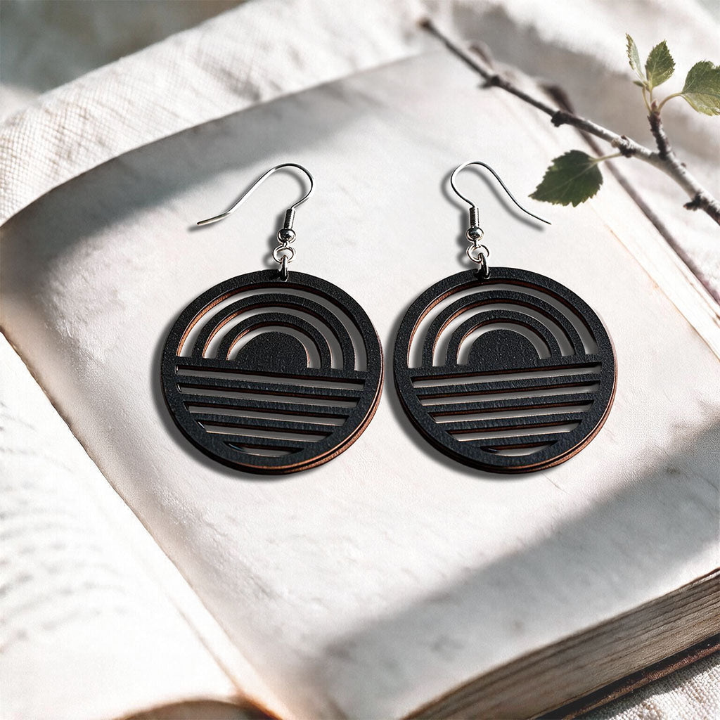 Black Sunrise plywood earrings made in Finland, photographed on a vintage book in natural sunlight