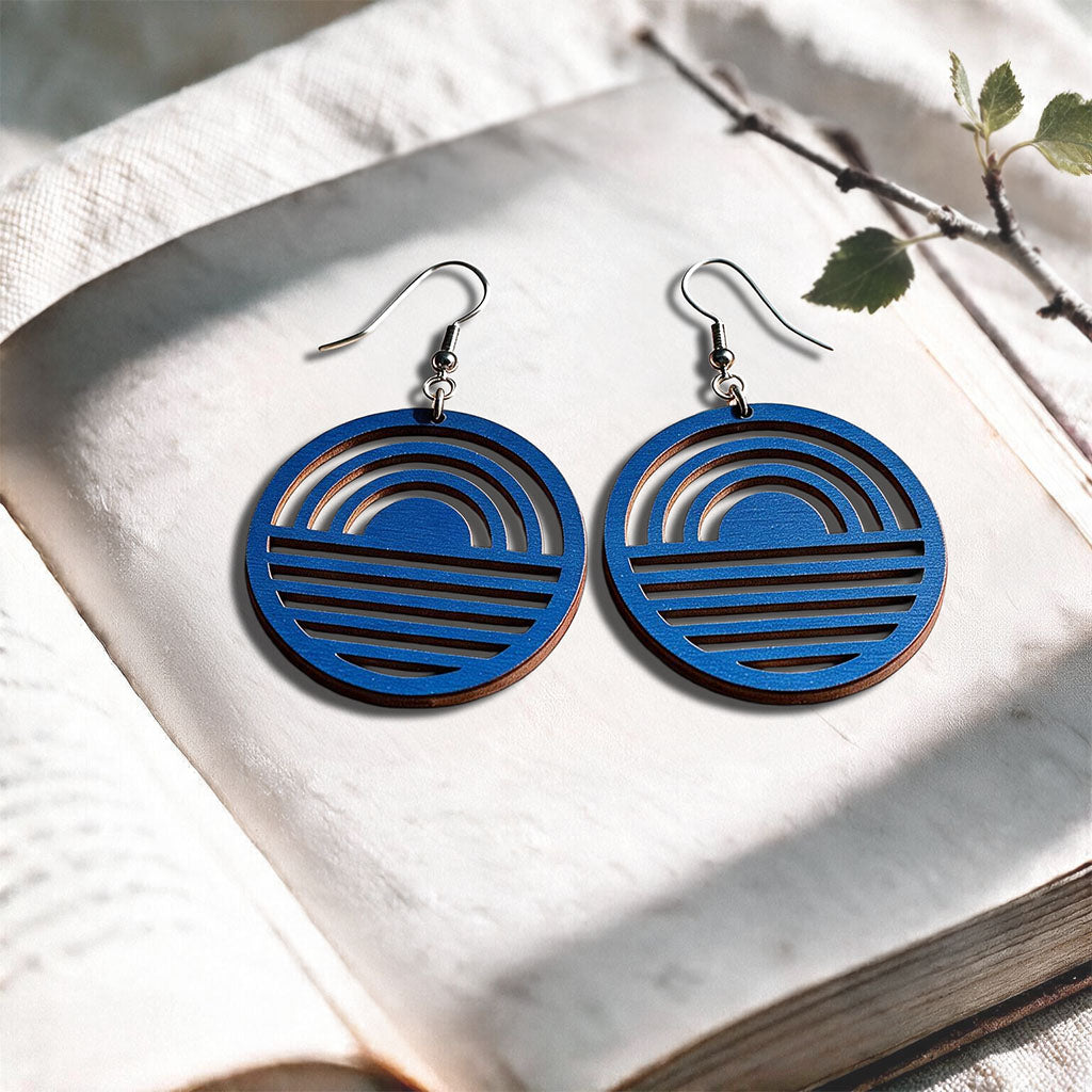 Blue Sunrise plywood earrings made in Finland, photographed on a vintage book in natural sunlight