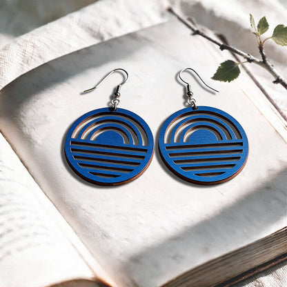 Blue Sunrise plywood earrings made in Finland, photographed on a vintage book in natural sunlight