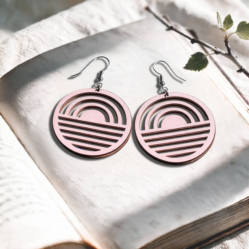 Light Pink Sunrise plywood earrings made in Finland, photographed on a vintage book in natural sunlight