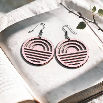 Light Pink Sunrise plywood earrings made in Finland, photographed on a vintage book in natural sunlight