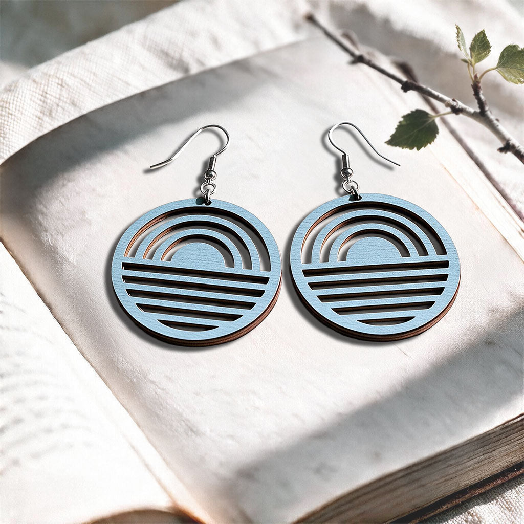 Light Blue Sunrise plywood earrings made in Finland, photographed on a vintage book in natural sunlight