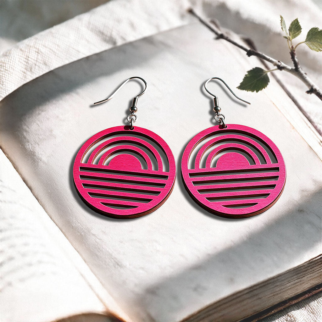 Raspberry Sunrise plywood earrings made in Finland, photographed on a vintage book in natural sunlight